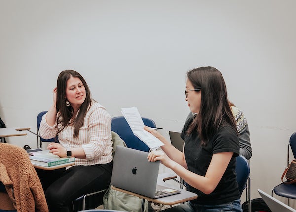 Two students participating in class. One student reads from a paper. 